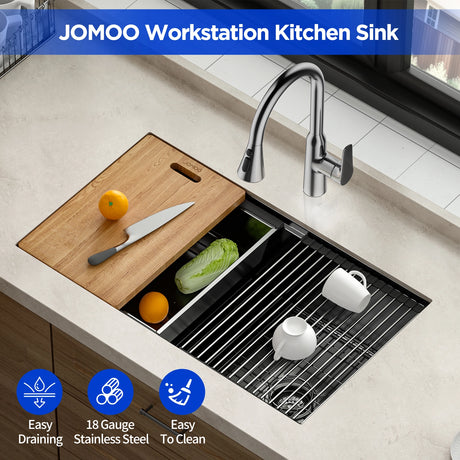Shows a JOMOO workstation kitchen sink with a bamboo cutting board placed on top, holding a knife and an orange. The sink features a sleek design with the JOMOO logo displayed at the top and highlights like "Easy Draining", "18 Gauge Stainless Steel", and "Easy To Clean" at the bottom.