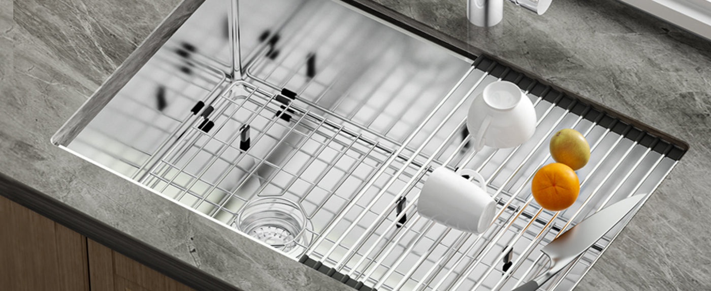 A close-up view of a sleek, modern JOMOO Premium 304 stainless steel kitchen sink with an integrated drainboard. The sink features a polished finish, a grid rack for drainage, and is styled with a white teacup and fresh citrus fruits, set against a gray marble countertop.