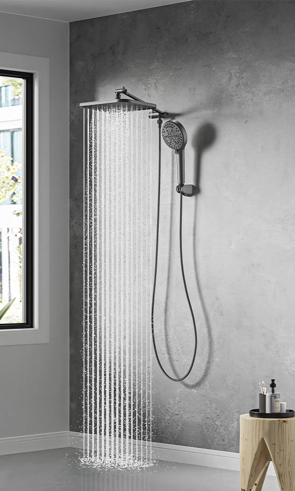 A tall JOMOO matte-black shower column features an overhead rainfall head and a handheld wand, both crisply silhouetted against light marble tiles.